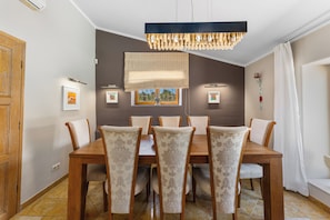 A dining area with a wooden table and chairs, a chandelier, and framed pictures on the walls.