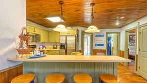 A kitchen with wooden ceiling, green cabinets, a central island with stools, and a refrigerator. - Beautiful, Bright Home Steps From Little Red River (Heber Springs)