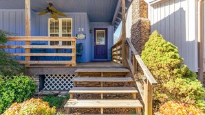 A wooden porch with a blue door, a wooden staircase, and a stone wall. - Beautiful, Bright Home Steps From Little Red River (Heber Springs)