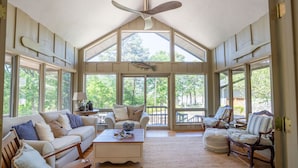 A spacious living room with a high ceiling, large windows, and a ceiling fan. - Greers Ferry Lakefront Home in Eden Isle (Heber Springs)