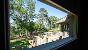 A view from a window overlooking a wooden deck with a railing, surrounded by trees and a clear sky. - Greers Ferry Lakefront Home in Eden Isle (Heber Springs)