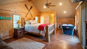 A cozy log cabin bedroom with a bed, a wooden headboard, a ceiling fan, a pool table, and a fish decoration on the wall. - Greers Ferry Lakefront Home in Eden Isle (Heber Springs)