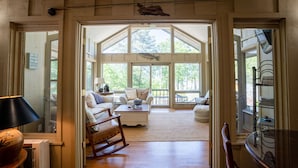 A spacious room with a large window, a wooden rocking chair, a white sofa, and a coffee table. - Greers Ferry Lakefront Home in Eden Isle (Heber Springs)