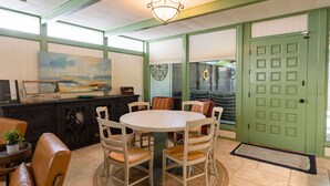 A dining area with a round table, chairs, and a bench. There is a painting on the wall, a cabinet with a mirror, and a green door.