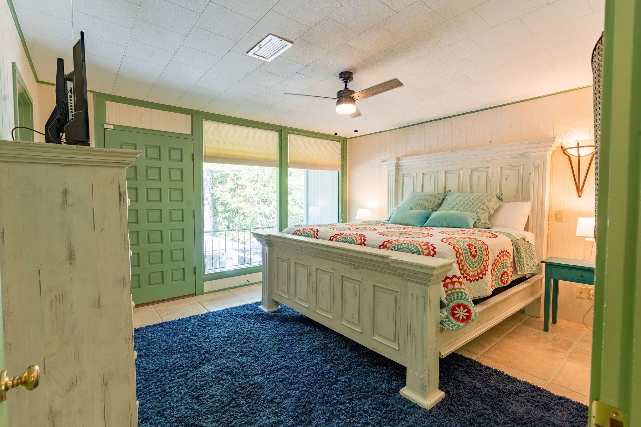 Une chambre à coucher avec un lit, un ventilateur de plafond, une porte verte et une fenêtre.