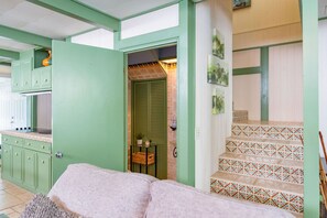 Una habitación con decoración verde, una zona de cocina, una escalera con peldaños estampados y una puerta que da a otra habitación.
