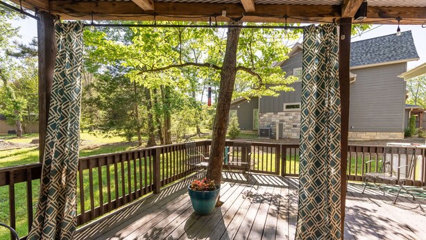 A covered outdoor deck with a wooden railing, a potted plant, and a view of a house in the background.