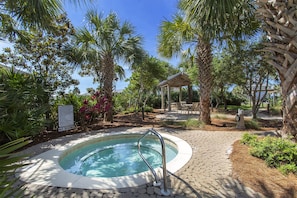 A pool area with a hot tub, surrounded by palm trees and a gazebo.