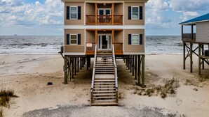 A two-story beach house with a wooden staircase leading to the entrance, located on stilts over the sand. - These are the Days - Gulf Beachfront, 5 Bedroom, 3 Full/3 Half Baths, Sleeps 15 (Dauphin Island)