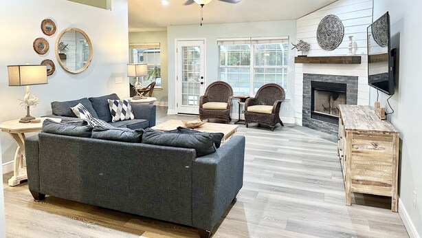 Ein geräumiges Wohnzimmer mit grauem Sofa, Korbstühlen, Kamin und Deckenventilator.