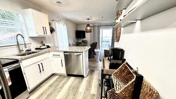 A modern kitchen with white cabinets, stainless steel appliances, and a wooden floor. - Emerald Hideaway 2 Bedroom Condo by RedAwning (Navarre)