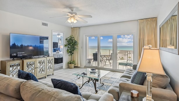 A living room with a television, sofa, and a balcony with a view of the ocean.