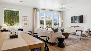 A modern living room with a wooden dining table, white sofa, and a flat-screen TV. - Sun-kissed At Desert Color 5 Bedroom Townhouse (St. George)