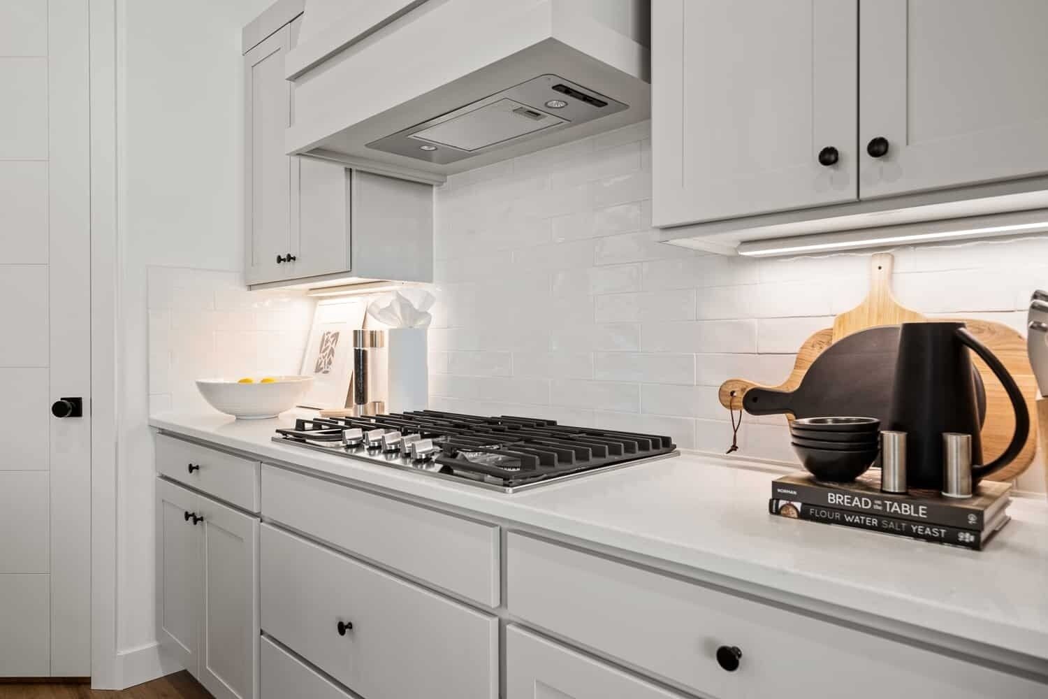 A modern kitchen with white cabinetry, a gas stove, and a bread table with kitchen essentials.