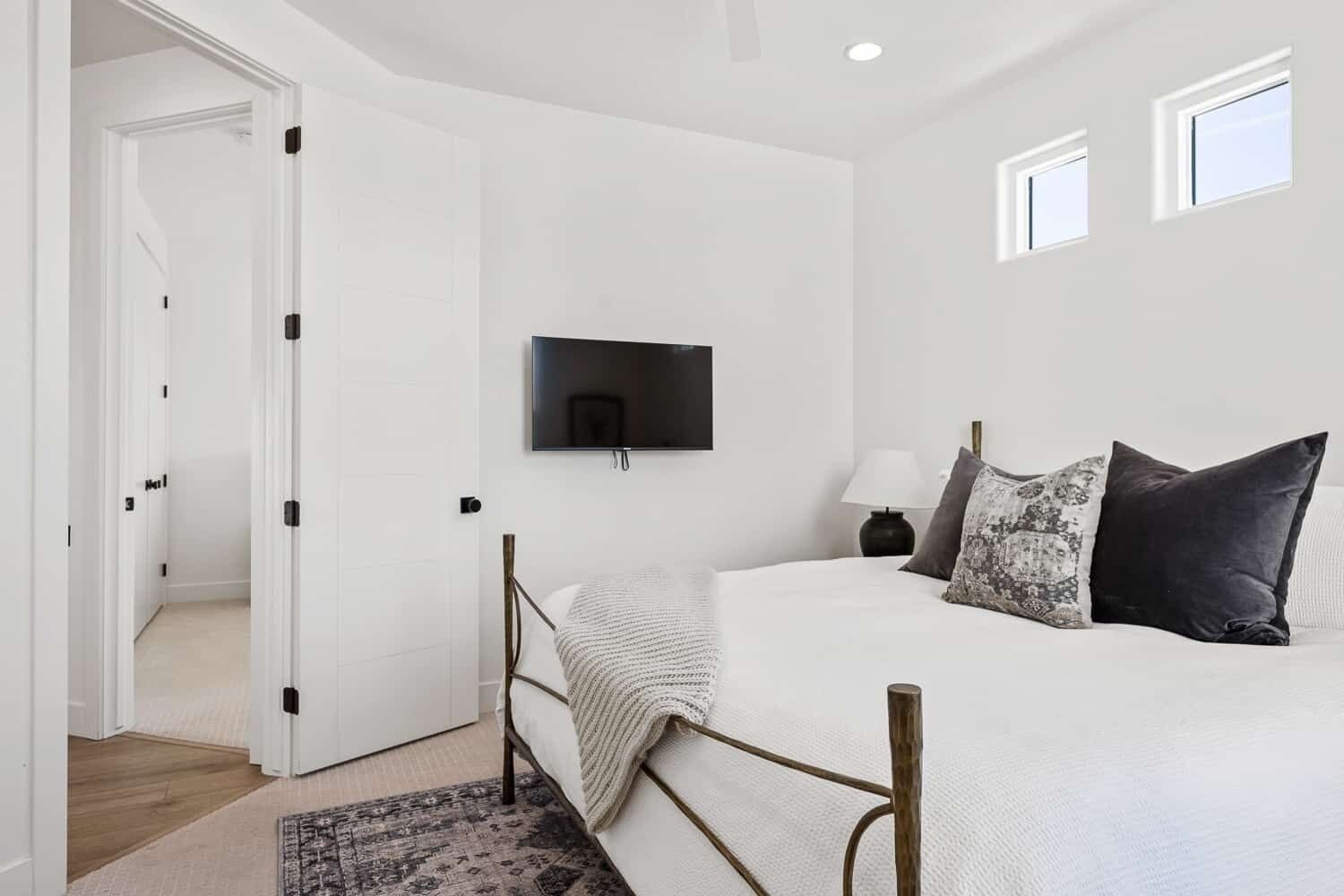 A bedroom with a bed, a TV mounted on the wall, a door, and a window.