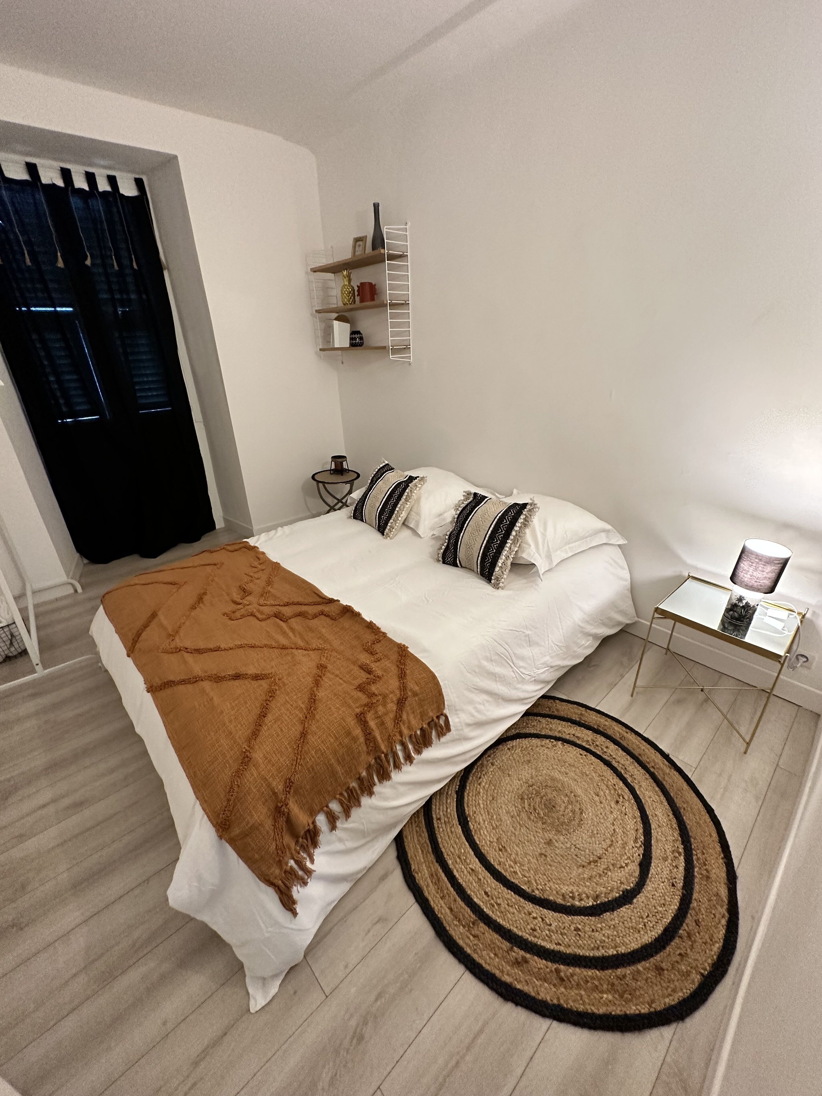 Un dormitori modern amb llit, tauleta de nit i una petita estant amb objectes decoratius.