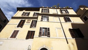 Un edificio a più piani con facciata gialla, numerose finestre con persiane e un portone con una targa porta numero.