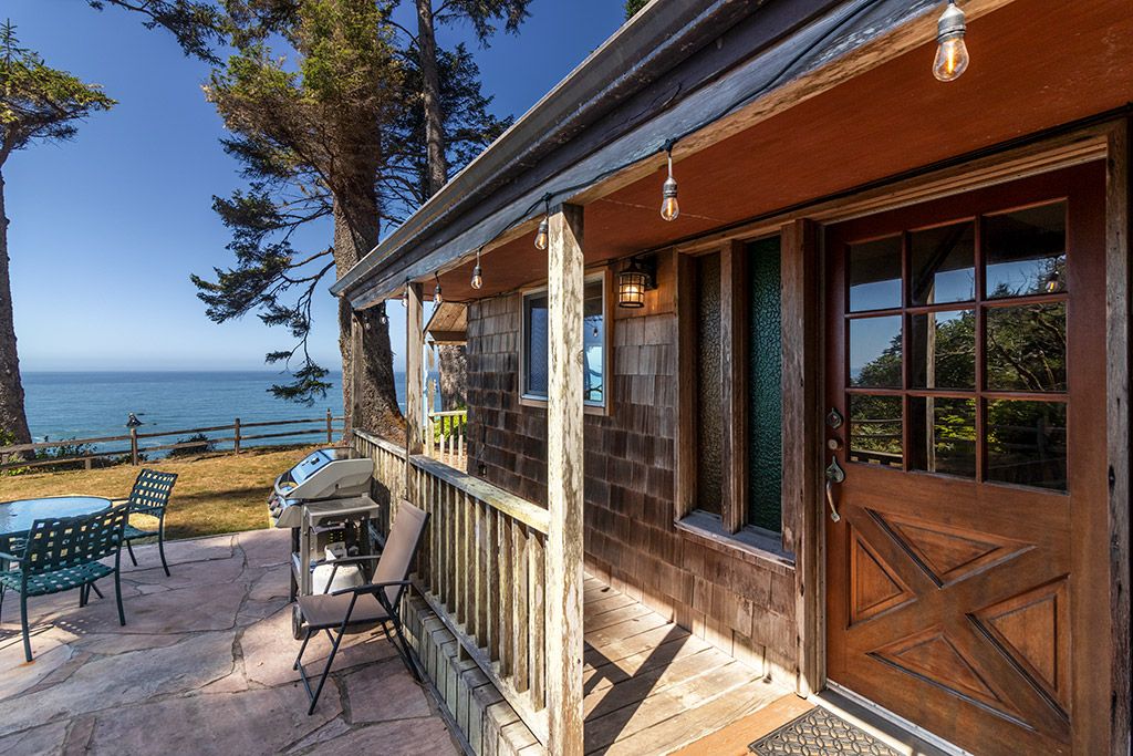 A wooden building with a porch, outdoor seating, and a view of the ocean.