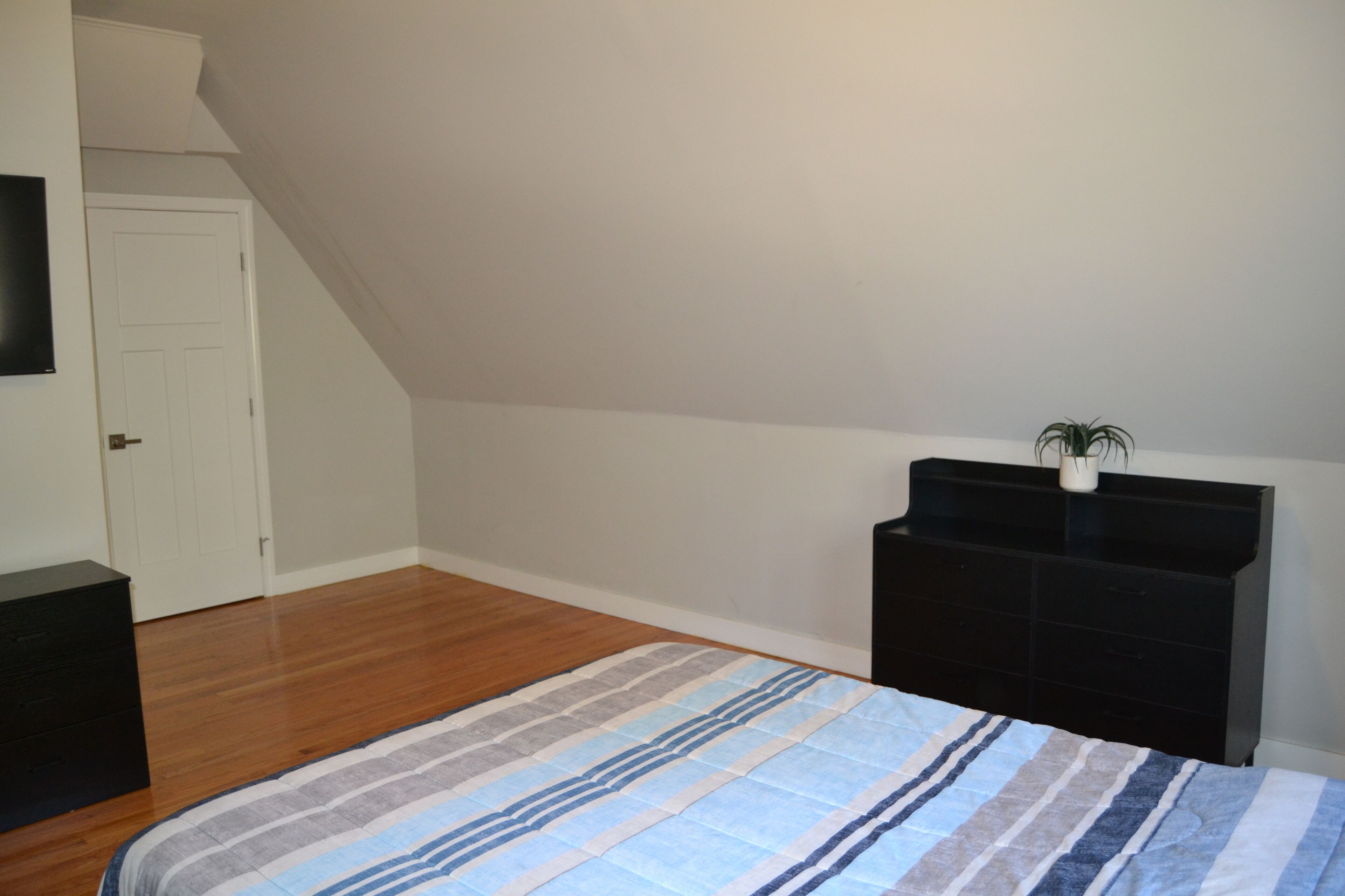 A bedroom with a bed, a dresser, a TV, and a door.