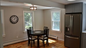 A dining area with a round table and chairs, a wall clock, and a refrigerator.