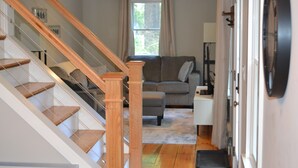 A staircase with wooden steps and glass railings, a gray sofa, a small table, and a door with a round mirror.