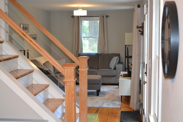 A staircase with wooden steps and glass railings, a gray sofa, a small table, and a door with a round mirror.