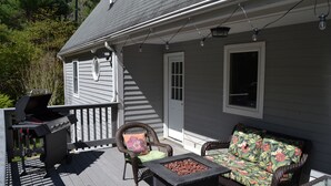 A covered outdoor deck with a grill, wicker furniture, and string lights.
