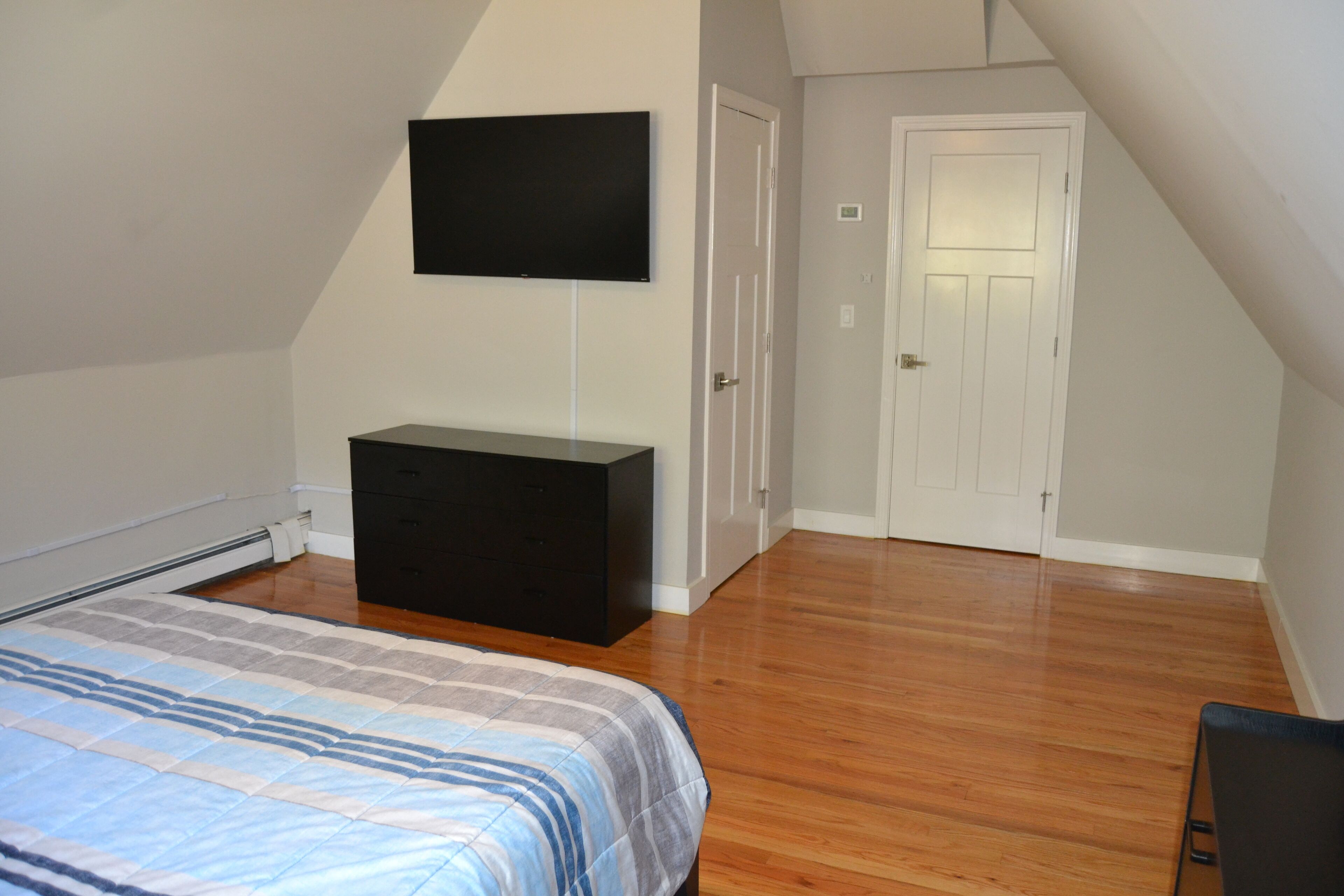 Un dormitorio con una cama, un aparador negro, un televisor en la pared y una puerta.