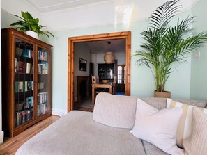 Ein gemütliches Wohnzimmer mit einer Couch, einem Bücherregal und einer großen Pflanze.