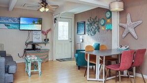 A cozy living room with a television, a ceiling fan, and a dining area with a table and chairs. - Pet Friendly , Beach Views on the Quiet East End of SJB ~ Sea Star (St. Joe Beach)
