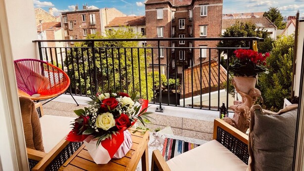 A balcony with a view of residential buildings, a wicker chair, a table with a bouquet of flowers, and a statue. - Luxury just 10 minutes from central Paris. Free Parking (Vitry-sur-Seine)