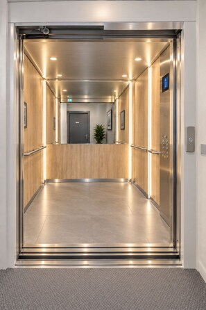 Interieur van een lift met een metalen afwerking, een handgreep en een bedieningspaneel aan de rechterkant.