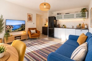 A modern living room with a sofa, a television, and a dining area with a table and chairs.