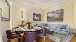 Un comedor con una mesa redonda para cuatro personas, rodeado de sillas moradas, un sofá y un tapete estampado.