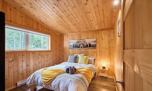 A wooden-paneled bedroom with a bed, pillows, a window, and a bear picture on the wall.
