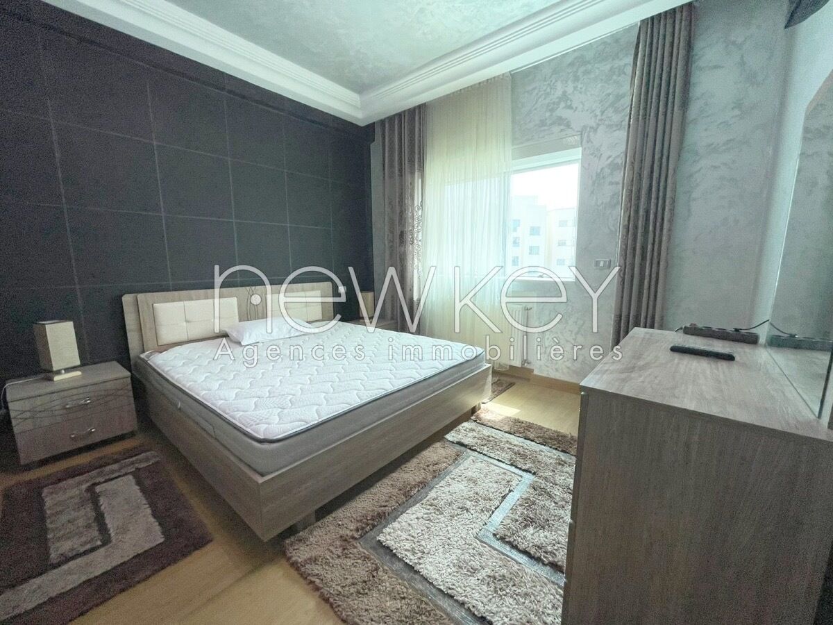 Une chambre à coucher moderne avec un grand lit, une table de chevet, une commode et une fenêtre avec des rideaux.