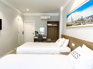 Hotellihuone, jossa on kaksi sänkyä, työpöytä, tuoli, vaatekaappi ja seinällä kaupunkimaisemaa esittävä taulu.