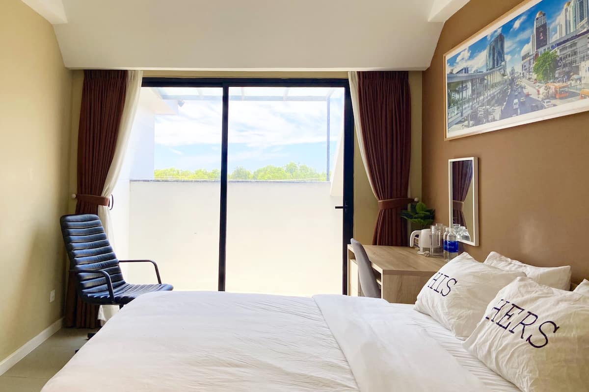 Una camera d'albergo con un letto, una scrivania, una sedia, un'ampia finestra con tende e un quadro appeso al muro.