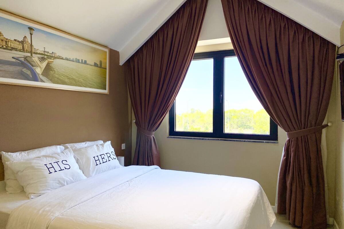Una camera da letto con un letto, due cuscini con scritte, un quadro e una finestra con tende.