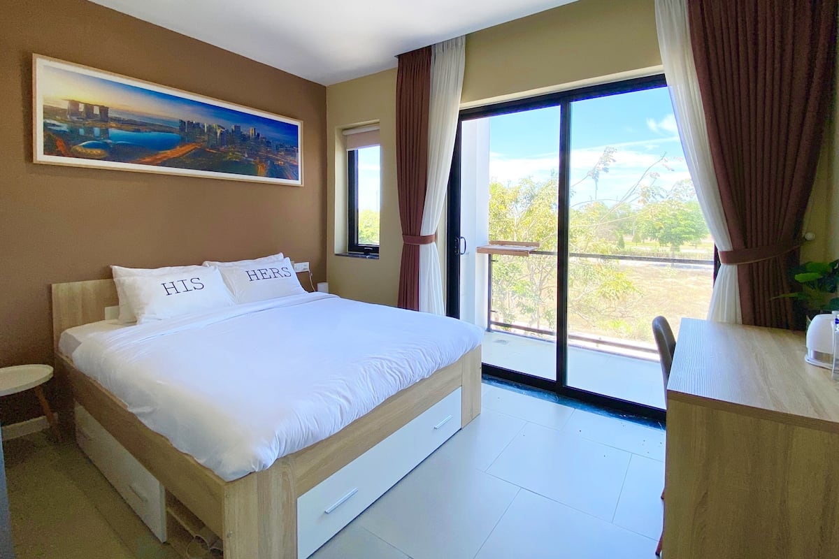 Una camera da letto con un letto grande, una scrivania, una finestra con tende e un quadro appeso al muro.