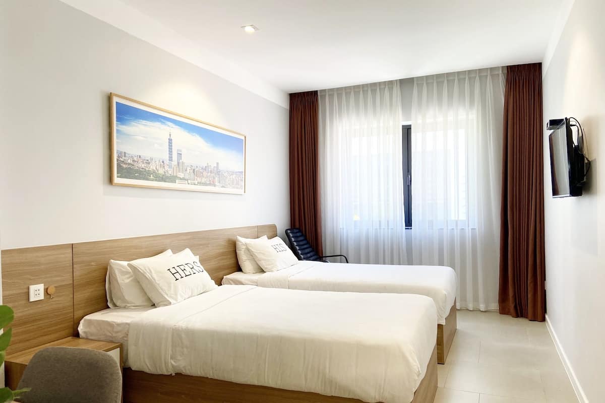 Una camera d'albergo con due letti, un quadro che raffigura un panorama urbano, una televisione e una finestra con tende.
