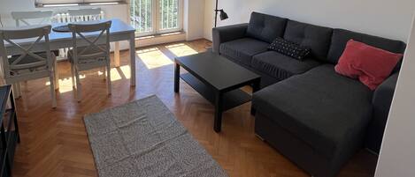 A modern living room with a sofa, coffee table, and a dining area with chairs and a table.