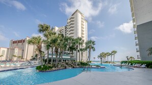 A resort pool area with palm trees, a clear sky, and a large building in the background. - Sunset views over the Gulf.  Beachside BEST.  The perfect getaway for two!   (Panama City Beach)