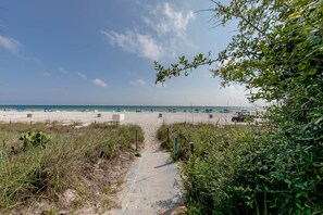 A sandy beach path leading to a beach with umbrellas and beach chairs.