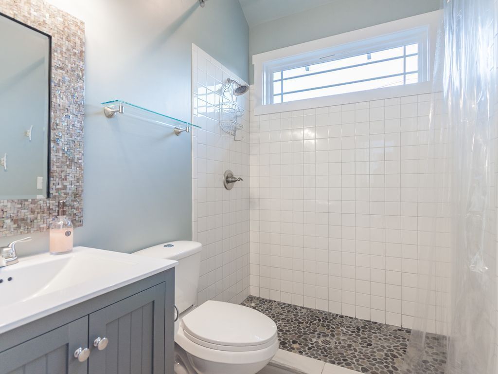 Une salle de bain avec des toilettes blanches, un lavabo et un espace douche doté d’un sol carrelé.