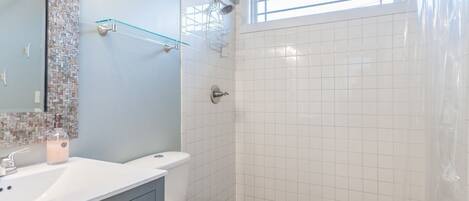 Une salle de bain avec des toilettes blanches, un lavabo et un espace douche doté d’un sol carrelé.