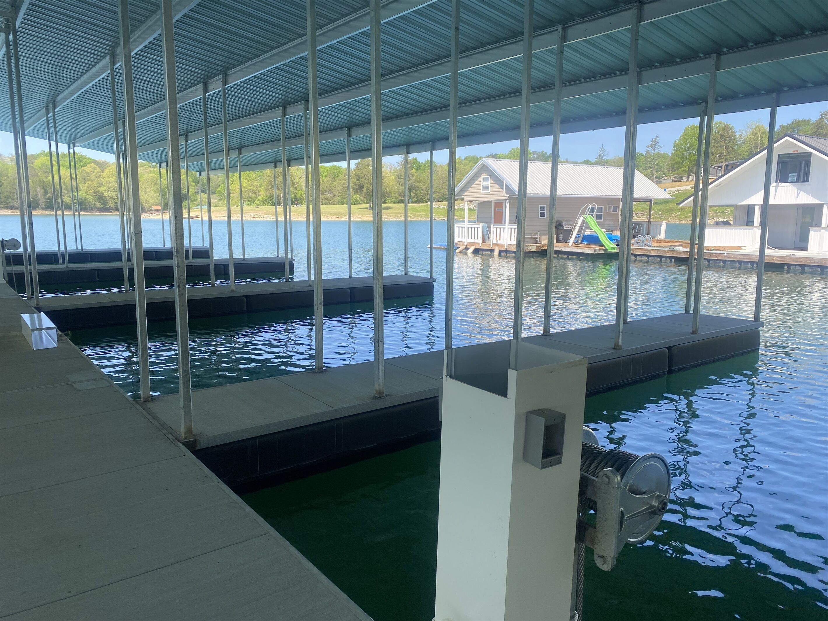 A covered swimming area with a view of a lake and houses in the background.