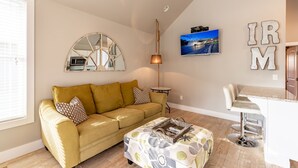 A living room with a sofa, ottoman, and a TV mounted on the wall.