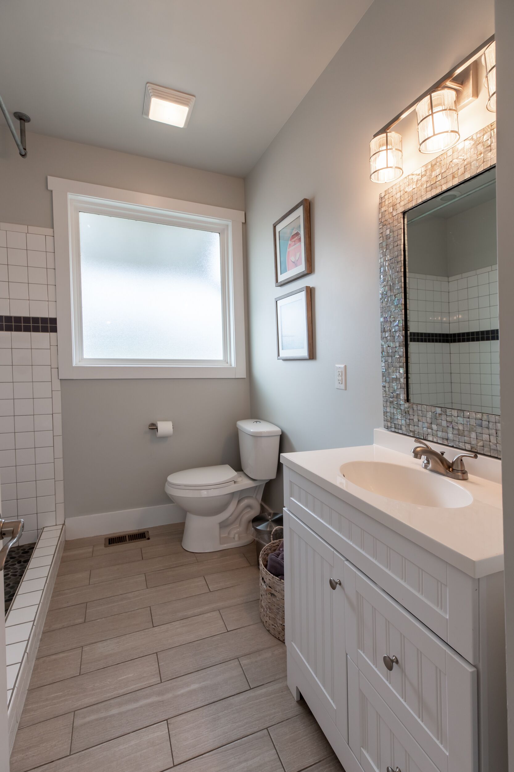 A modern bathroom with a toilet, sink, and vanity. There is a window providing natural light and a mirror above the sink.