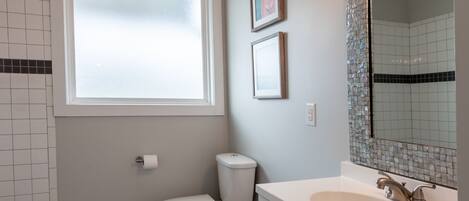 A modern bathroom with a toilet, sink, and vanity. There is a window providing natural light and a mirror above the sink.